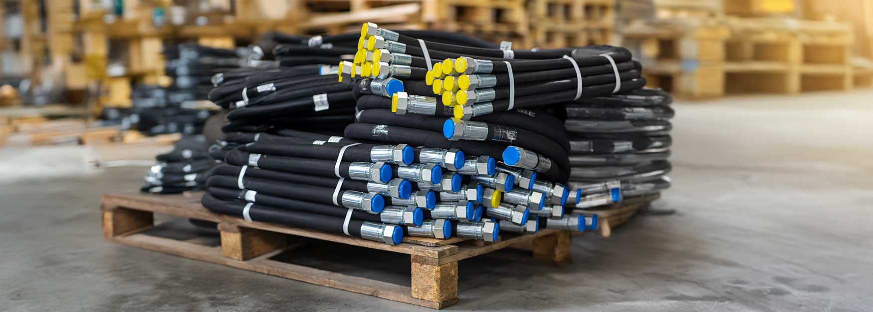 Mehrere Hydraulikschläuche auf einer Europalette in einer Lagerhalle.