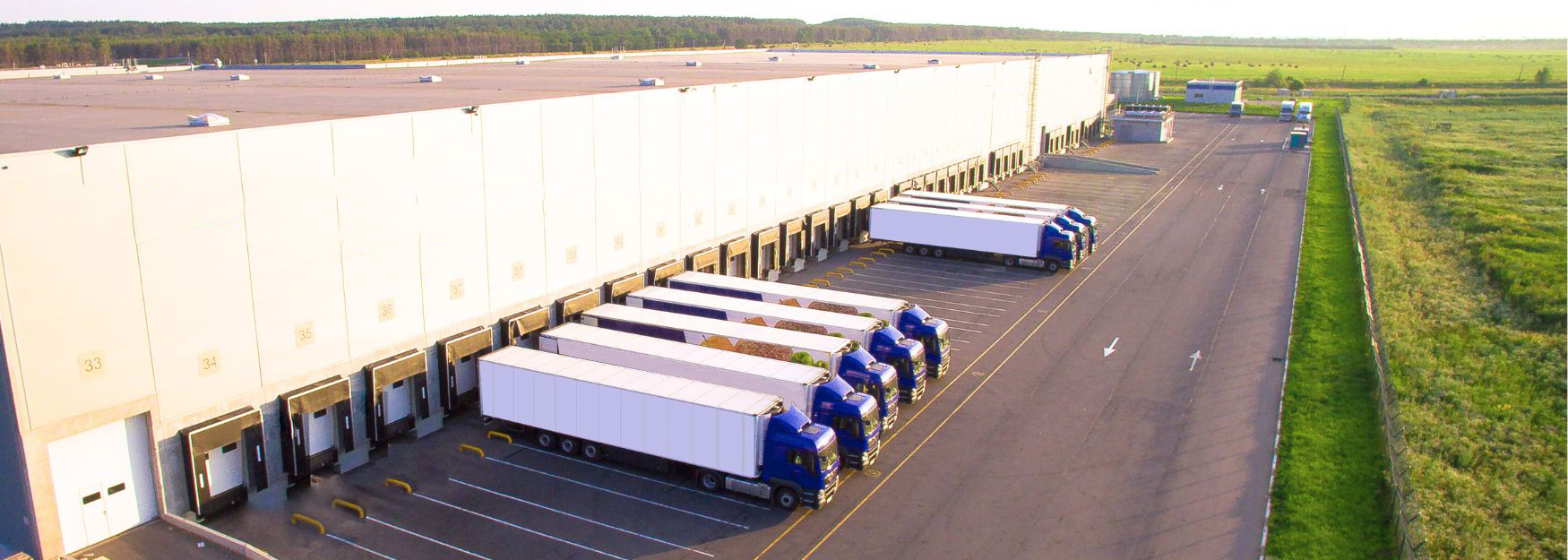 Ein Speditions- und Logistikunternehmen betreibt eine große Halle, vor der zahlreiche LKWs beim Be- und Entladen von Handelswaren stehen.