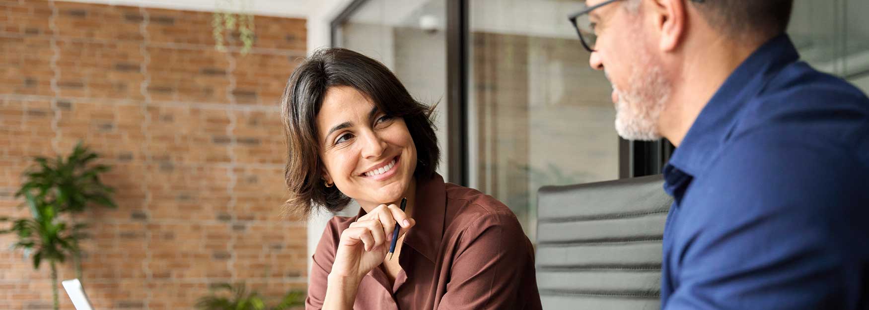 Zwei Personen sitzen an einem Tisch mit Laptop und Dokumenten in einem modernen Büro.